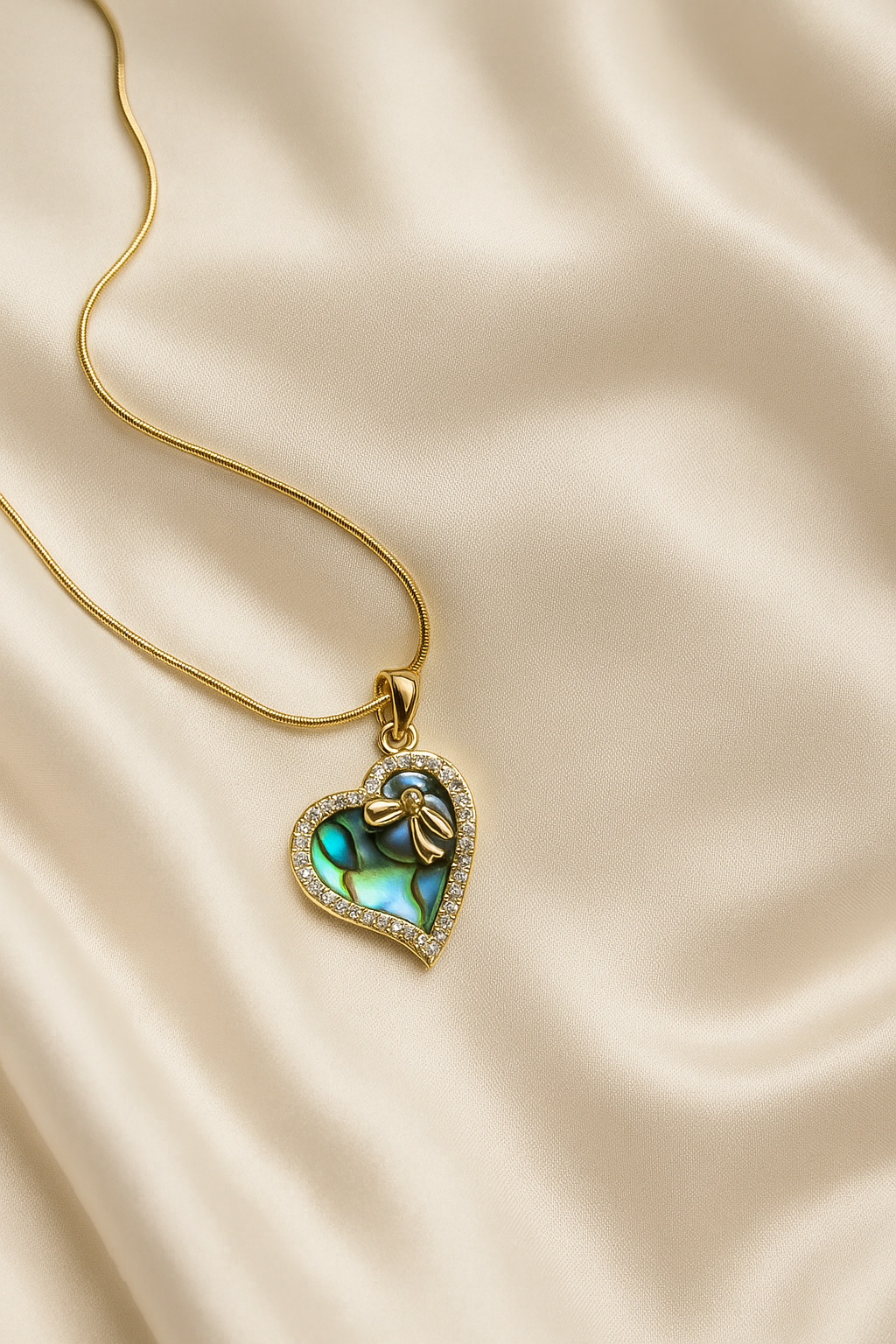 Heart-shaped pendant with green gemstone on a gold chain against a beige fabric background